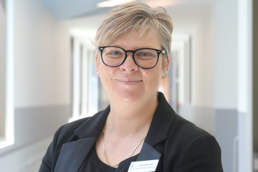 A blonde woman with glasses stands in the corridor of Frankston Hospital smiling